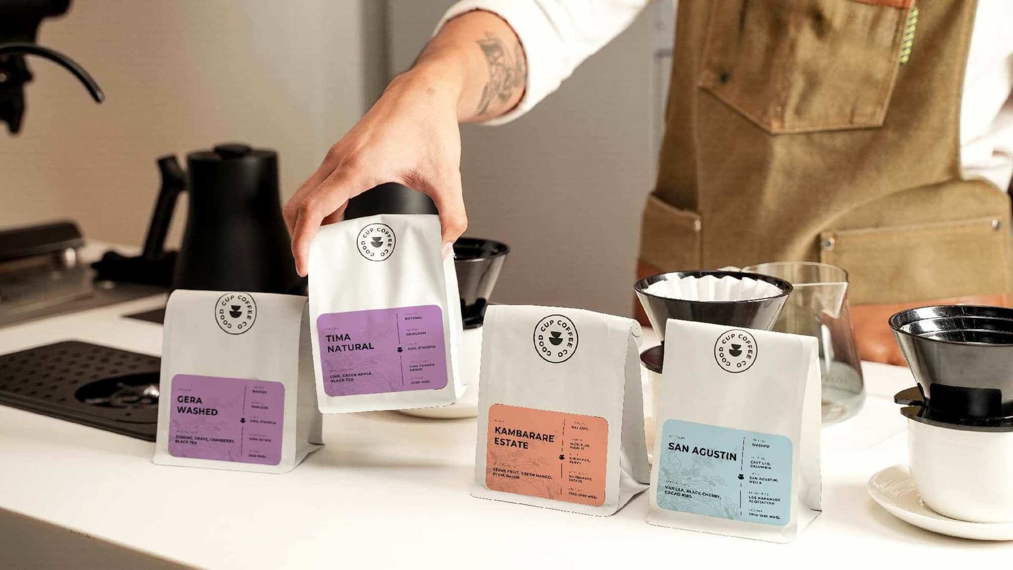 Four Good Cup coffee bags with colour-coded origin labels on a café counter