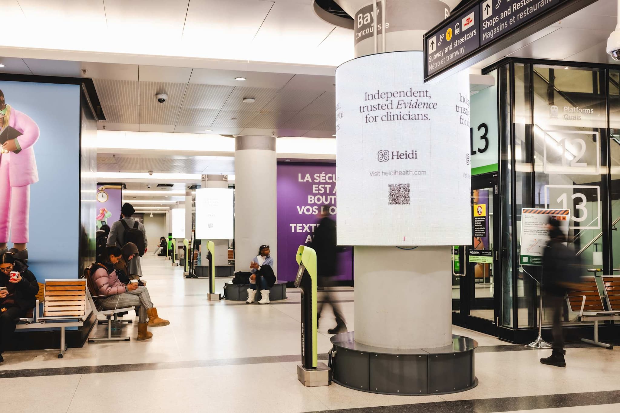 Heidi ad wrapped around a pillar in a busy transit concourse, reading “Independent, trusted Evidence for clinicians.”
