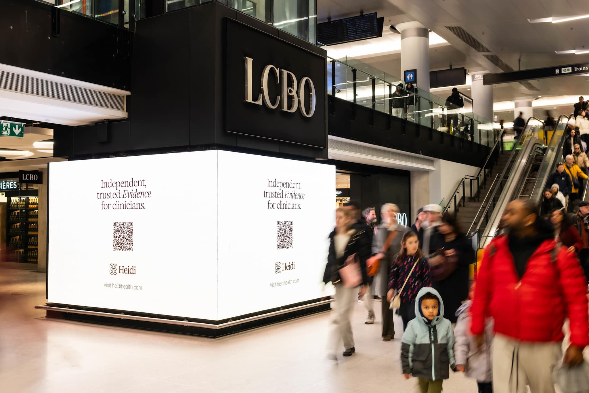 Illuminated Heidi ads on the corner of an LCBO store as commuters walk past