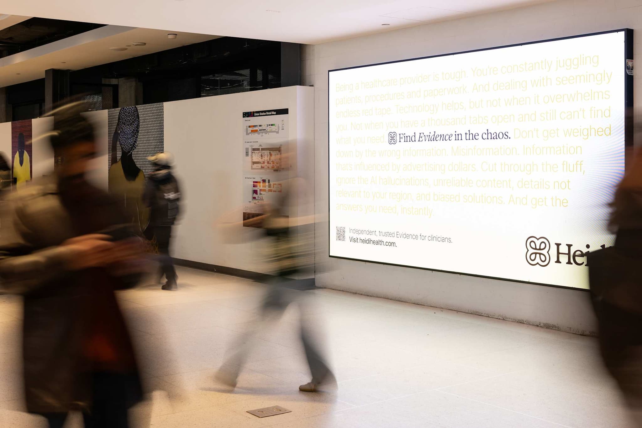 Large backlit Heidi wall ad with commuters blurred in motion