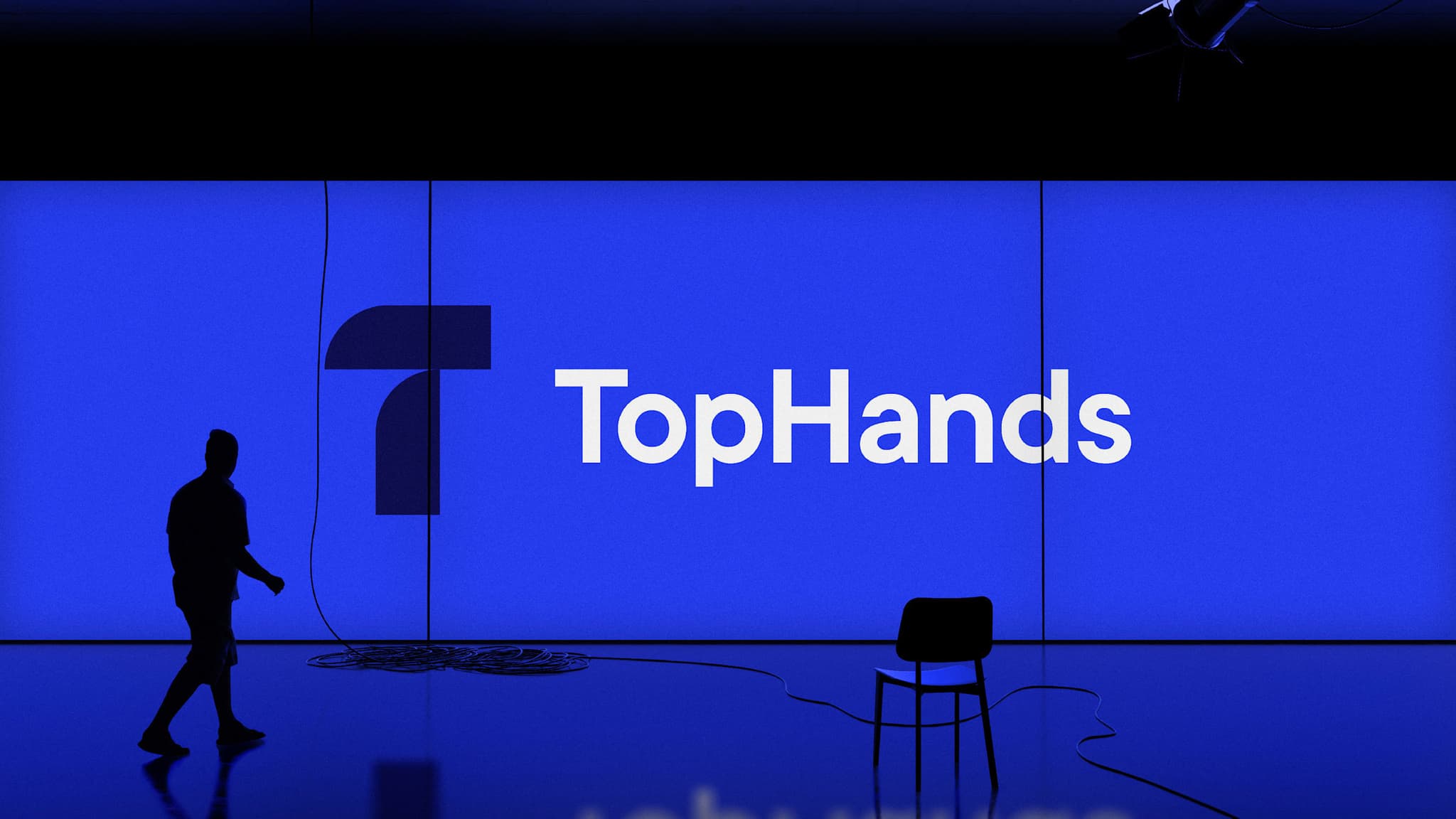 Silhouetted figure walking across a stage in front of a large TopHands logo
